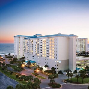 A multi-story hotel with a central courtyard, surrounded by palm trees and a parking area.
