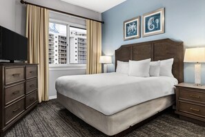 A hotel room with a large bed, a dresser, a TV, and a window with curtains.