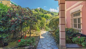 A stone pathway leading through a garden with various plants and a building with a window on the right. - CASA FLAMINIA - Panorama, Relaxation, and Parking (Ruta)