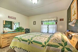 Ein Schlafzimmer mit Bett, Kommode, Spiegel und einem Fenster mit Vorhängen.