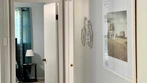 En gang med en dør til et værelse, et billede i ramme på væggen og et lille bord med en lampe.
