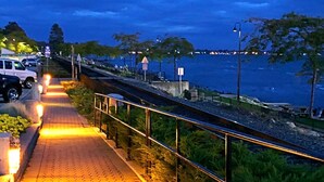 Une promenade pavée longe un plan d’eau, avec une rambarde d’un côté et une rangée de véhicules garés de l’autre.