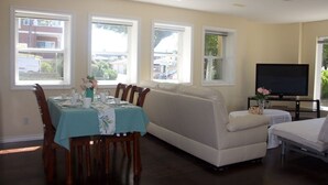Un coin repas avec une table dressée pour quatre personnes, un canapé, un téléviseur et de grandes fenêtres donnant sur l’extérieur.