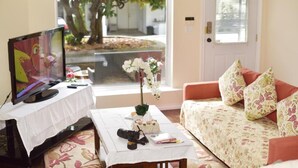 Un salon avec une télévision posée sur une table, un canapé à motifs floraux et une fenêtre donnant sur des arbres et un immeuble.