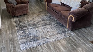 Ein Wohnzimmer mit einem braunen Sessel, einem braunen Sofa mit weißer Decke und einem gemusterten Teppich.