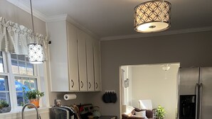 Eine moderne Küche mit weißen Schränken, Edelstahlgeräten und einem gemusterten Teppich, der in einen Wohnbereich mit Sofa und Couchtisch führt.
