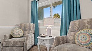 A living room with two grey armchairs, a white side table with a lamp, and teal curtains. - Three Minutes to White Sand Beach! (Panama City Beach)