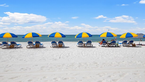 A beach with rows of blue and yellow beach umbrellas and lounge chairs facing the ocean. - Three Minutes to White Sand Beach! (Panama City Beach)