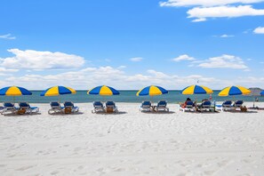Ein Strand mit blauen und gelben Strandliegen und Sonnenschirmen, die zum Meer ausgerichtet sind.