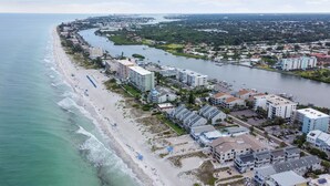 An aerial view of a coastal town with a beach, a river, and several buildings including hotels. - Waterfront views - steps from the Beach! (Indian Shores)