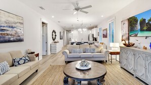 A spacious living room with a large round coffee table, a beige sofa, and a dining area with a white table. - Moorings 31 - Sunset Spectacular<br>The Moorings at Jekyll Harbor Marina (Jekyll Island)