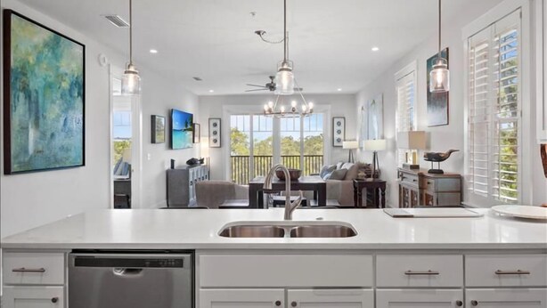 A modern kitchen with a central island, stainless steel appliances, pendant lighting, and a view to the outdoors.