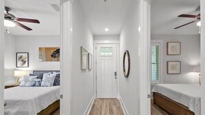 A hallway with two bedrooms, each with a bed, a ceiling fan, and a door at the end.