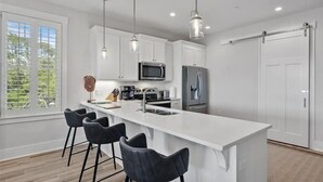A modern kitchen with white cabinets, a large island with bar stools, stainless steel appliances, pendant lighting, and a sliding door.