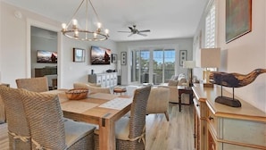 A spacious dining area with a wooden table and woven chairs, a chandelier, and a ceiling fan.