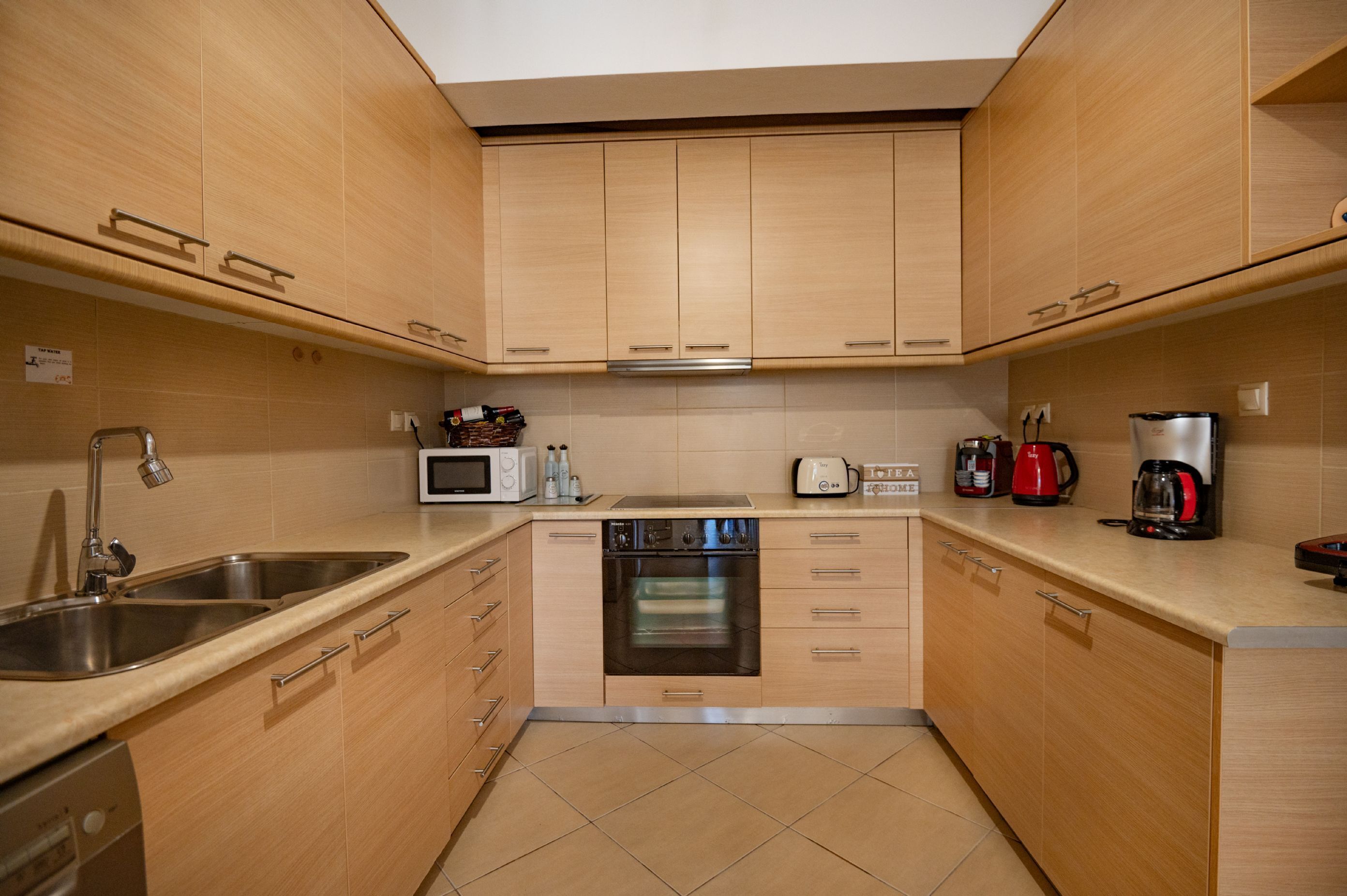 A compact kitchen with wooden cabinets, a built-in microwave, an oven, a coffee maker, and a sink.