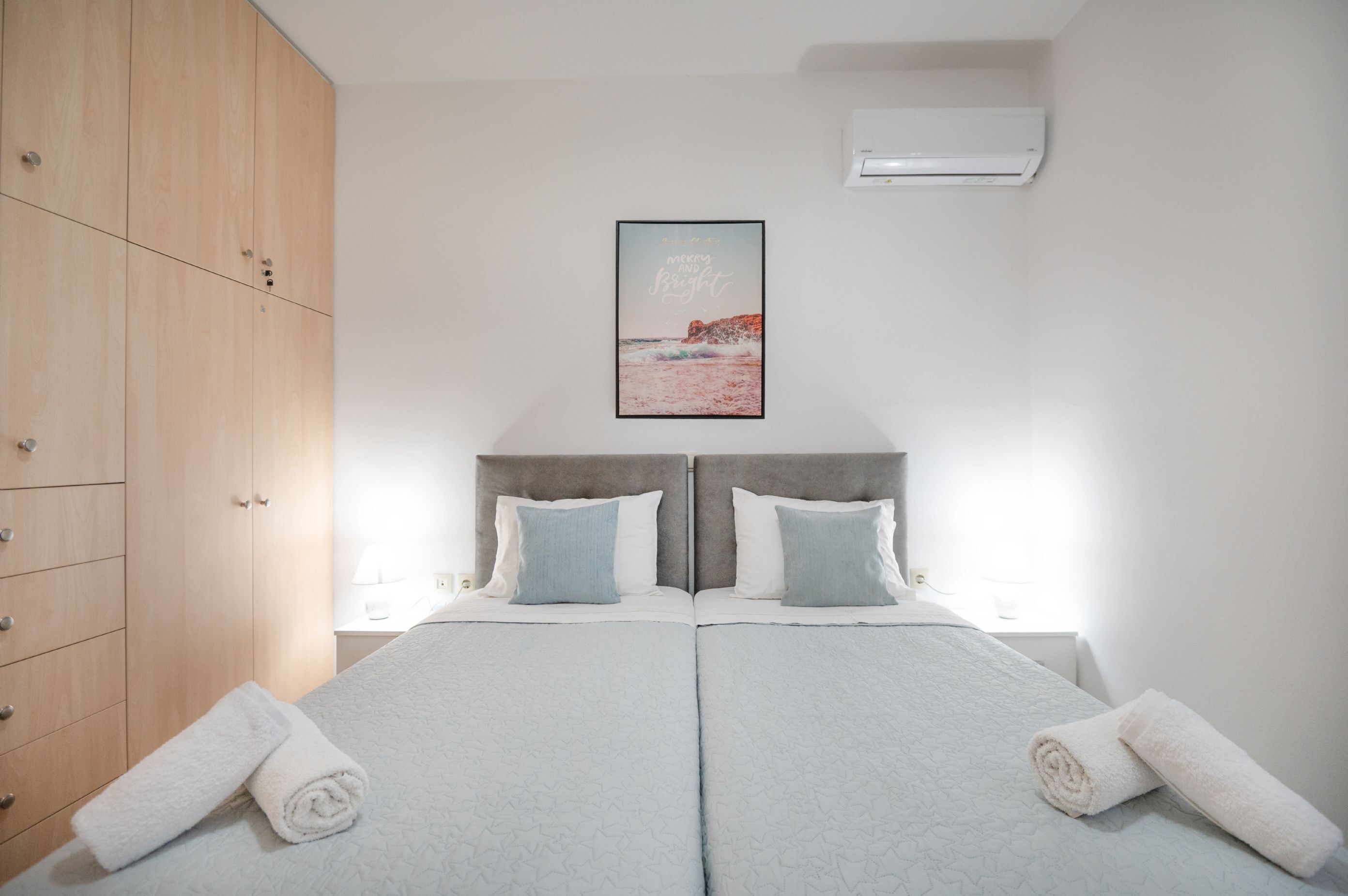 Un lit double avec deux oreillers, une armoire en bois, un tableau encadré accroché au mur et une serviette roulée posée sur le lit.