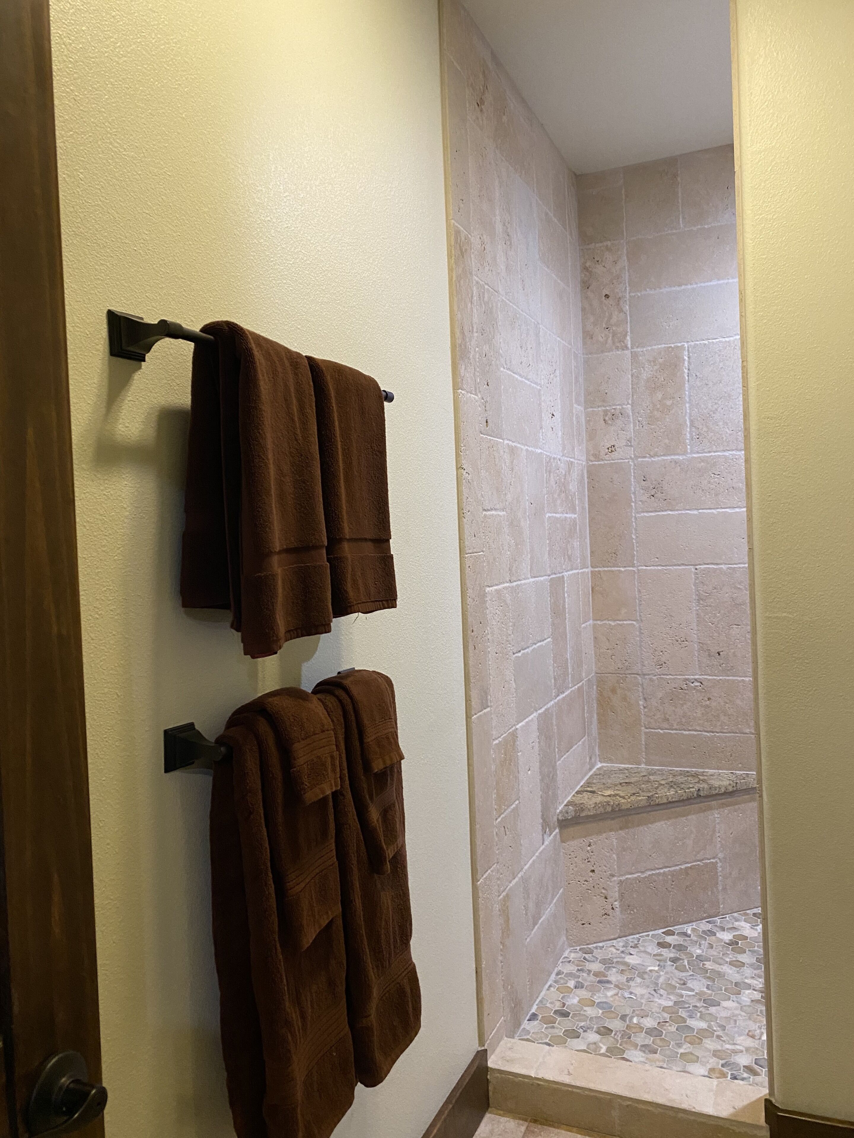A bathroom with two towels hanging on a rack, a tiled shower area, and a small tiled floor.