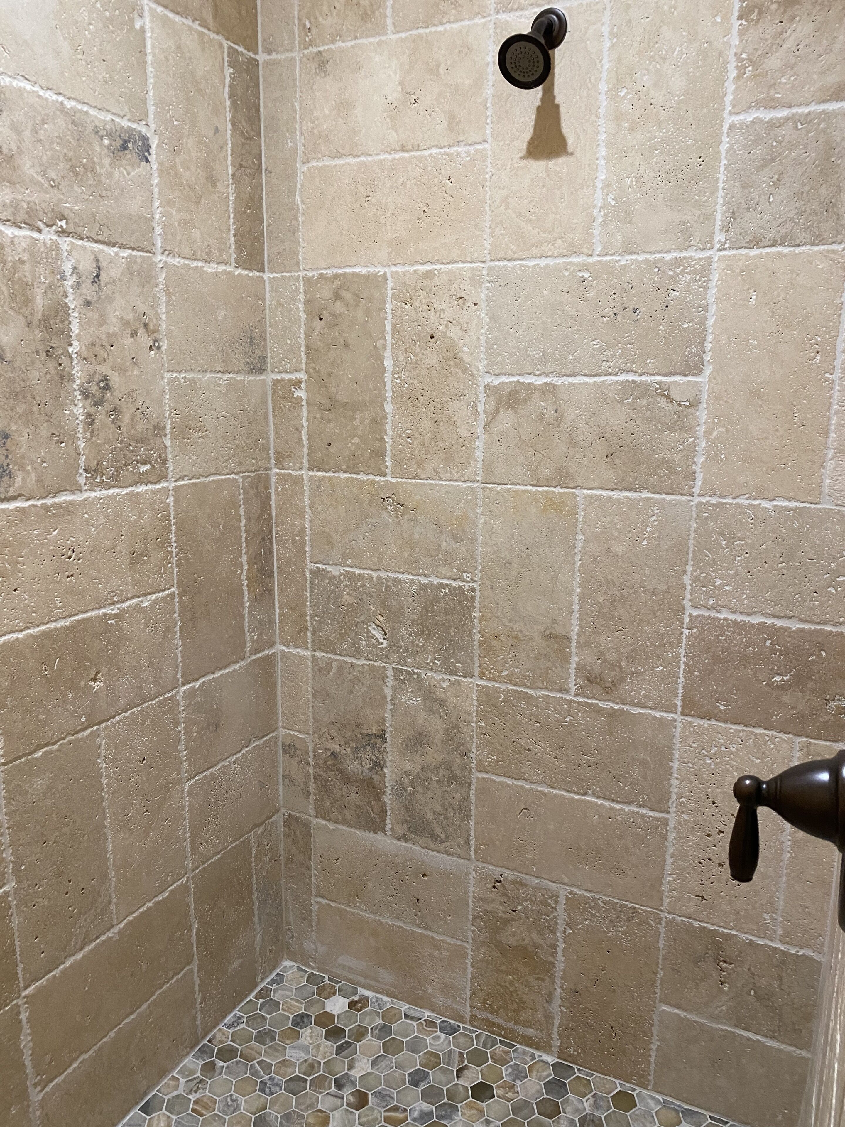 A shower with beige tiles and a mosaic floor.