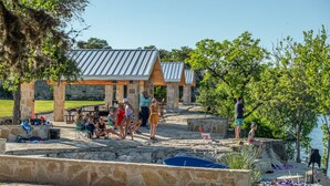 A stone patio with outdoor seating, a pool, and a covered area with a metal roof. - The River Lodge (Uvalde)
