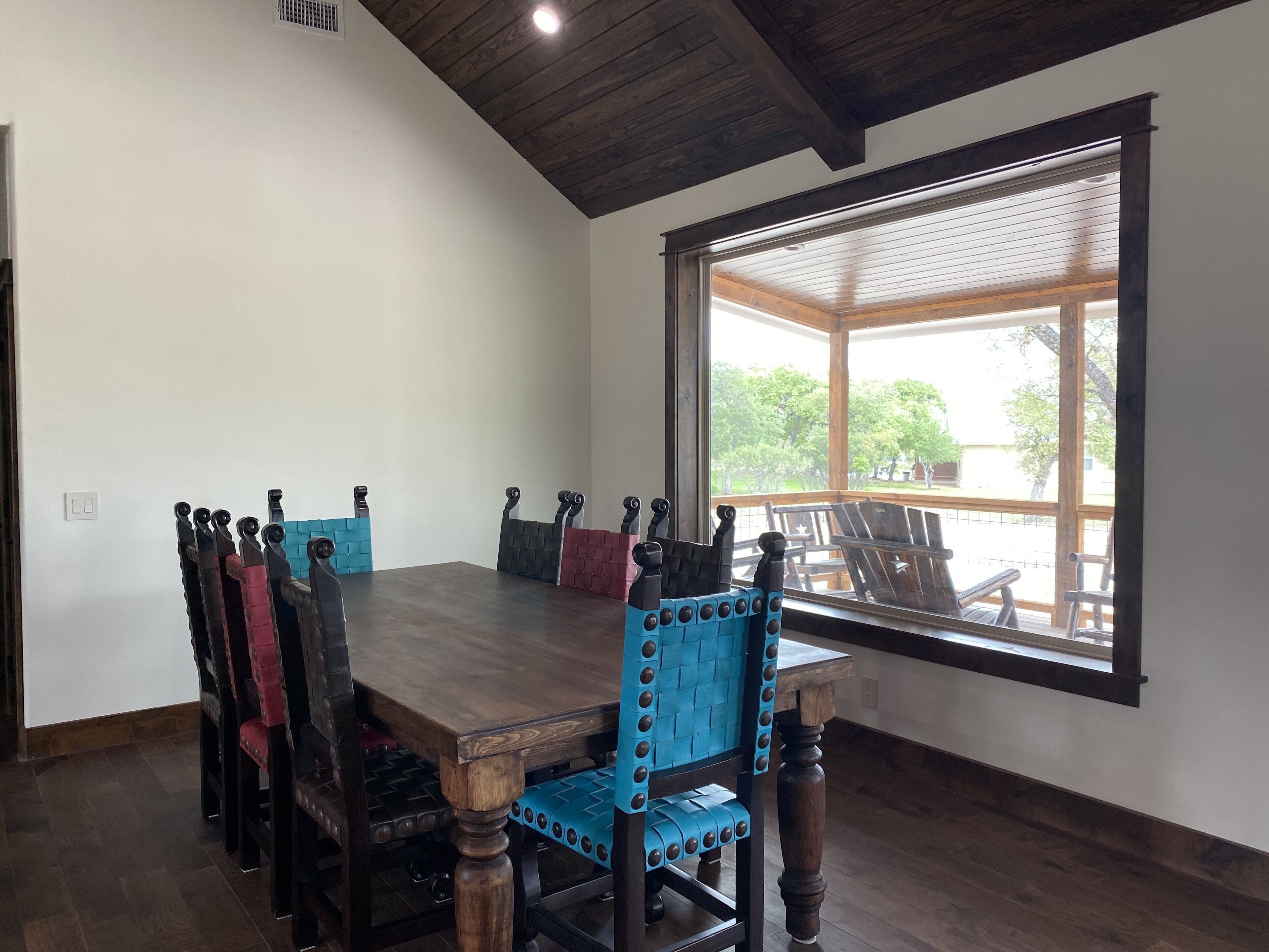 Un comedor con una mesa y sillas de madera, un ventanal con vista a árboles y un techo con vigas de madera.