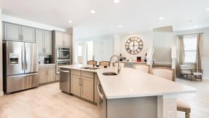 Una cocina moderna con electrodomésticos de acero inoxidable, una isla central con lavamanos y un reloj de pared grande.