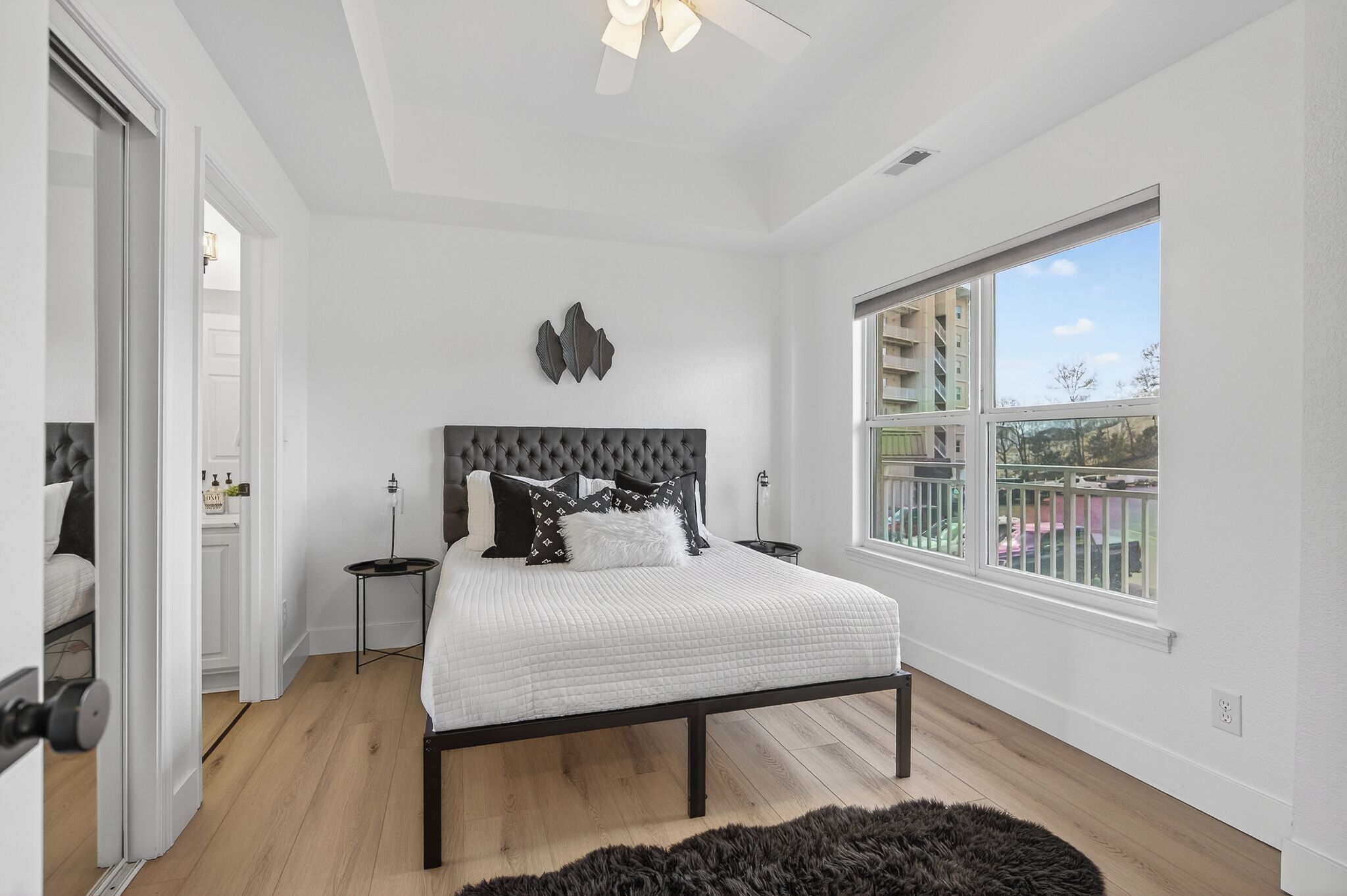 Quarto com cama, mesas de cabeceira, ventilador de teto, janela e vista para o exterior.