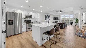 A modern kitchen with stainless steel appliances, a large island with bar stools, and a view to the outside.