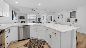 A modern kitchen with white cabinetry, a dishwasher, a large island, and a ceiling fan.