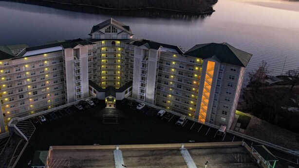 A multi-story hotel with a central courtyard, parking, and a view of a lake at dusk.