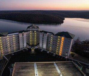 Ett hotell med flera våningar, en central innergård, parkering och utsikt över en sjö i skymningen.