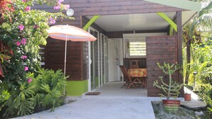 Une maison en bois avec un patio couvert, une table avec des chaises et une plante en pot.