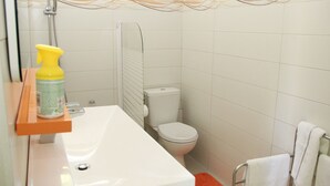 Une salle de bain avec un lavabo, des toilettes et une douche, le tout de couleur blanche.