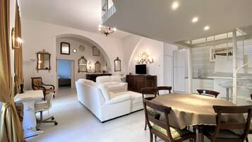 A spacious living area with a white sofa, a dining table with chairs, and a staircase leading to an upper level.