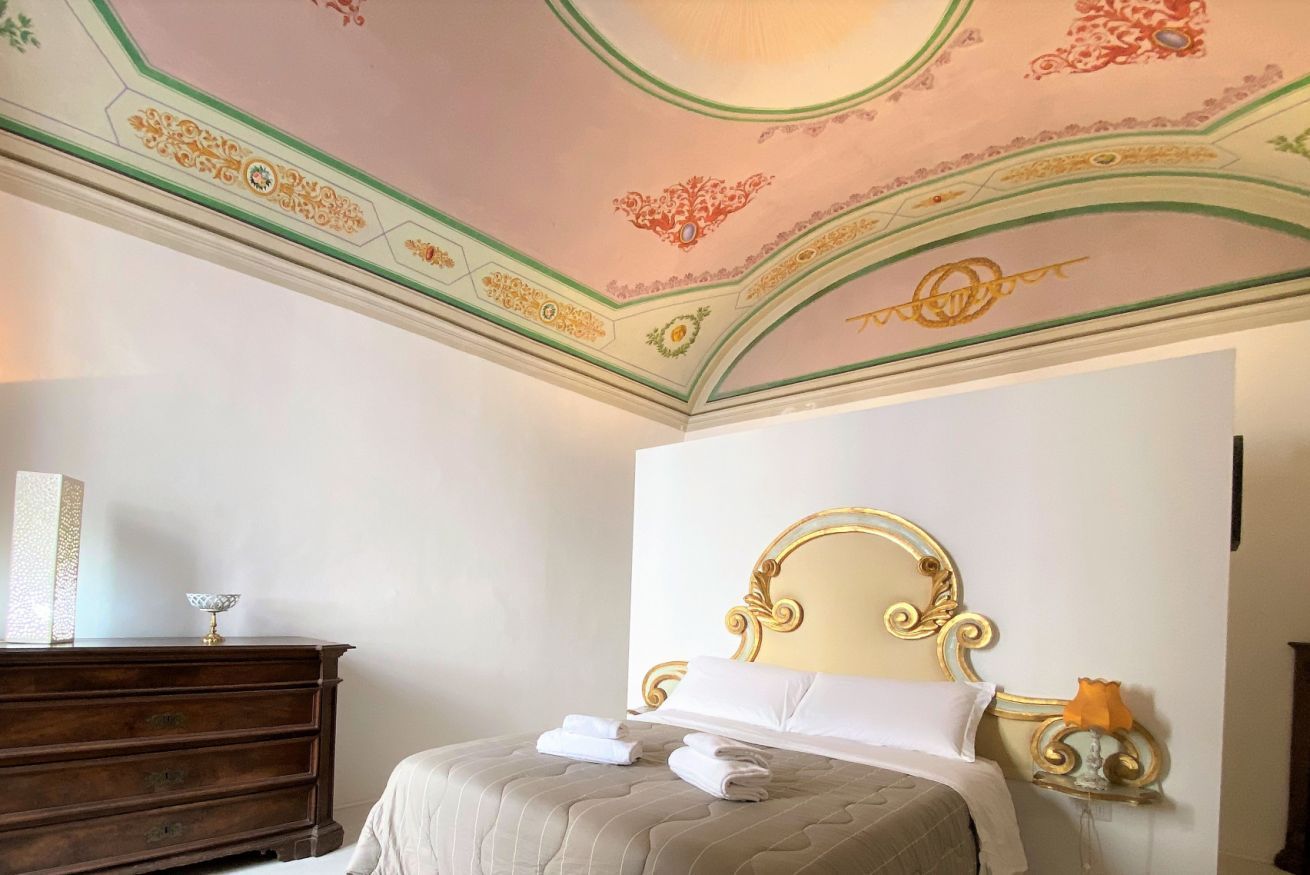 Una camera d'hotel con un letto, una cassettiera e un soffitto decorato.