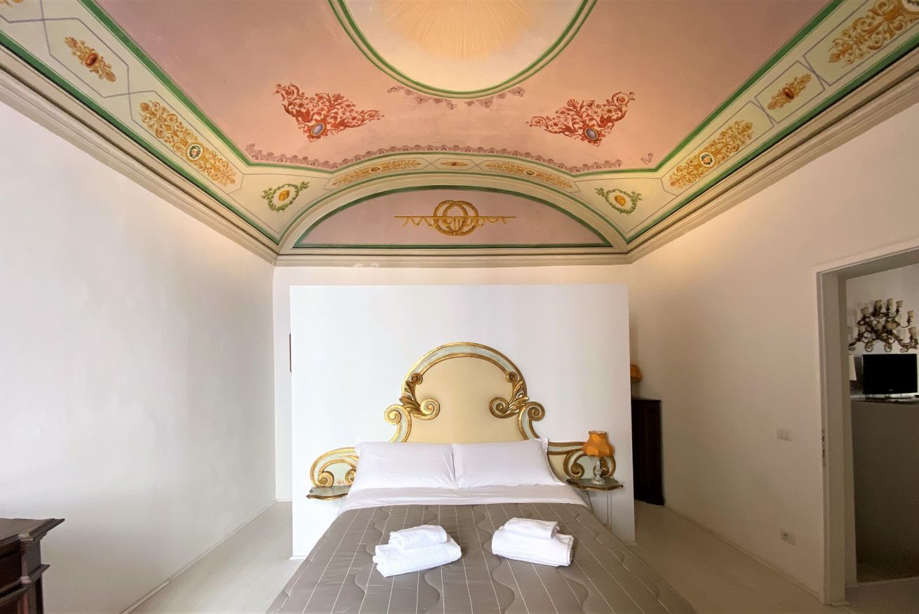 Ein Hotelzimmer mit einem großen Bett, einer verzierten Decke und einem kleinen Tisch mit einer Lampe.