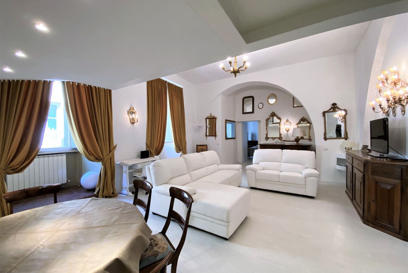 A spacious living room with a large white sectional sofa, a dining table with chairs, and a TV on a wooden cabinet.