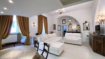 A spacious living room with a large white sectional sofa, a dining table with chairs, and a TV on a wooden cabinet.