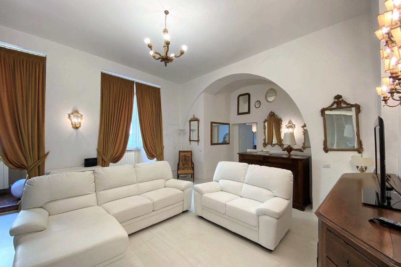 A spacious living room with two white sofas, a chandelier, and a wooden cabinet.