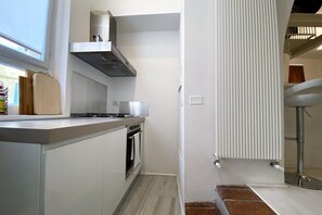 A modern kitchen with a built-in oven, a stainless steel range hood, and a window providing natural light.