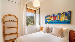 A bedroom with a bed, a wooden ladder, a window with a view of the countryside, and a colorful painting on the wall. - Villa Alberto - Country Relax (Puntalazzo)