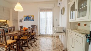 A dining area with a wooden table and chairs, a kitchen with white cabinets, a microwave, and a tiled floor. - Villa Alberto - Country Relax (Puntalazzo)