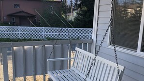 Une balançoire blanche suspendue à une terrasse en bois blanc, avec une clôture en treillis blanc en arrière-plan.