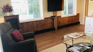 Un salon avec un canapé, une table basse en verre, un téléviseur posé sur un meuble et une cheminée.