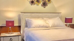 Un lit bien fait, avec du linge de lit blanc et un plaid décoratif. Il y a deux tables de chevet avec des lampes, et un élément décoratif mural au-dessus du lit.