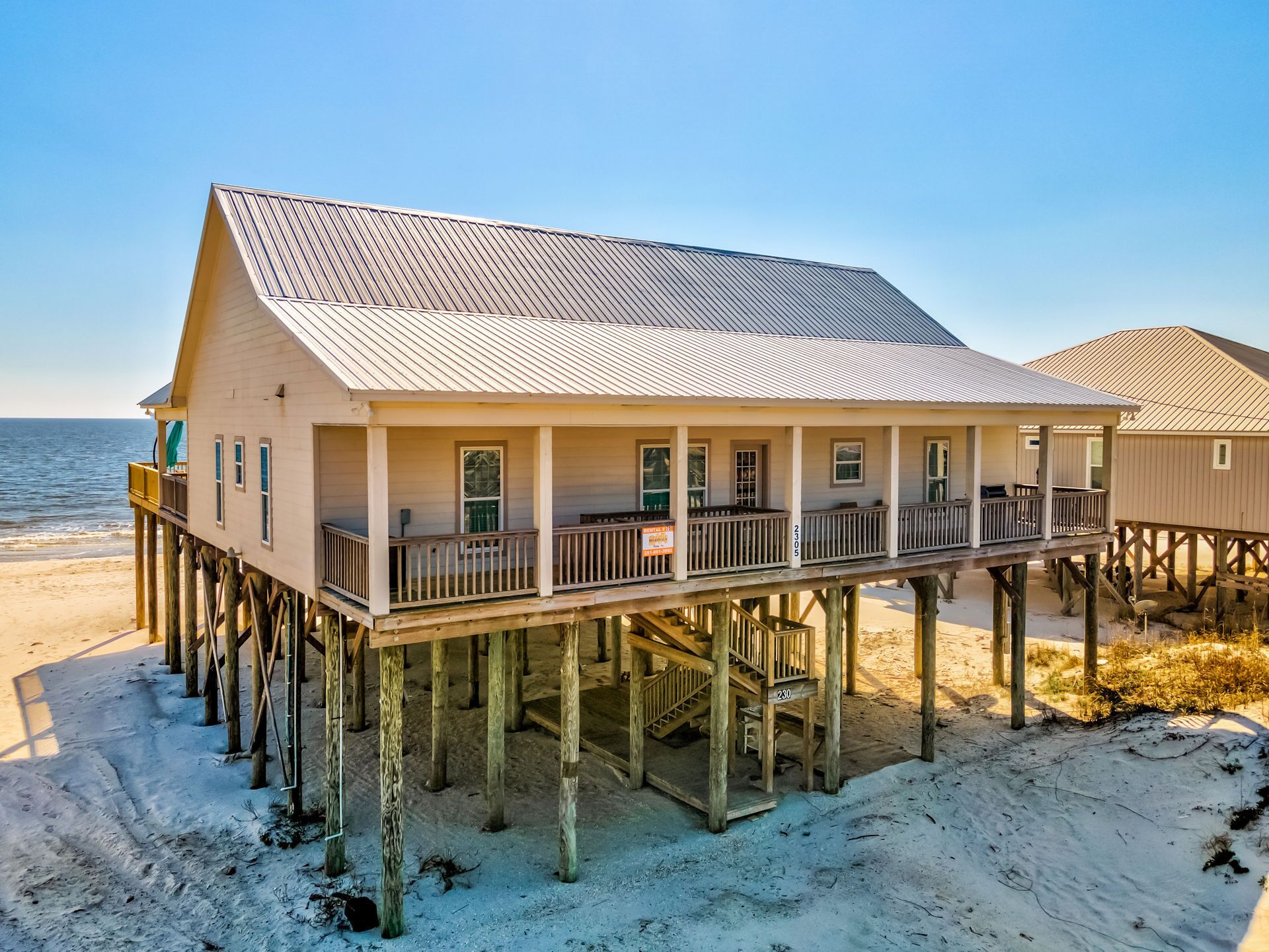 A beachfront house with a balcony, wooden deck, and a view of the ocean.