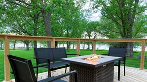 Una terraza al aire libre con una mesa para fuego, sillas negras y una pérgola de madera.