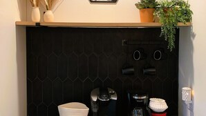 Una cocina con un salpicadero hexagonal negro, una cafetera, un hervidor, una cesta y una planta en maceta.