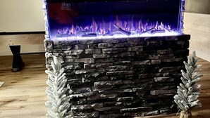 Una chimenea de piedra con llama azul, flanqueada por dos árboles de hoja perenne.