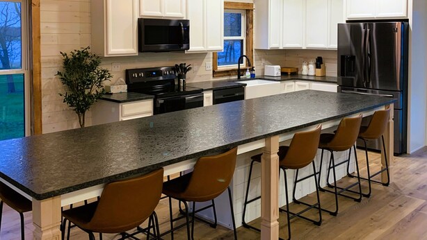 Una cocina moderna con armarios blancos, una isla grande con taburetes de bar, un refrigerador de acero inoxidable e iluminación colgante.